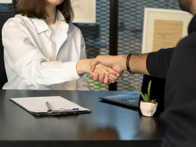 Two professionals shaking hands across a desk after a hiring conversation